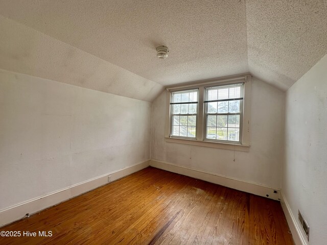 bonus room with visible vents, a textured ceiling, lofted ceiling, and hardwood / wood-style flooring