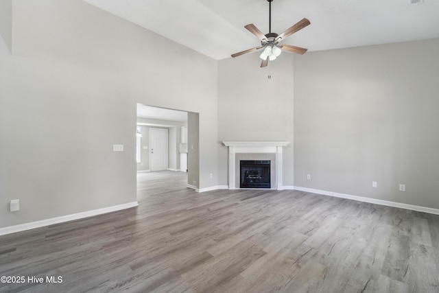 142 Burton Rd, Southport, NC 28461 - unfurnished living room with ceiling fan, a tiled fireplace, wood finished floors, high vaulted ceiling, and baseboards