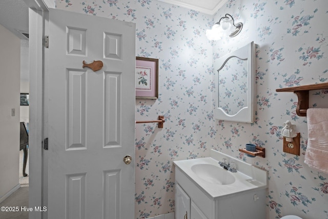 bathroom with crown molding, wallpapered walls, and vanity