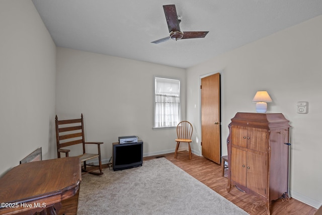 living area featuring baseboards, a ceiling fan, and wood finished floors