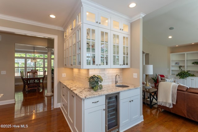 bar with ornamental molding, wine cooler, ornate columns, dark wood-type flooring, and a sink