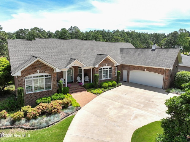 view of front of house with a garage, roof with shingles, brick siding, a porch, and driveway