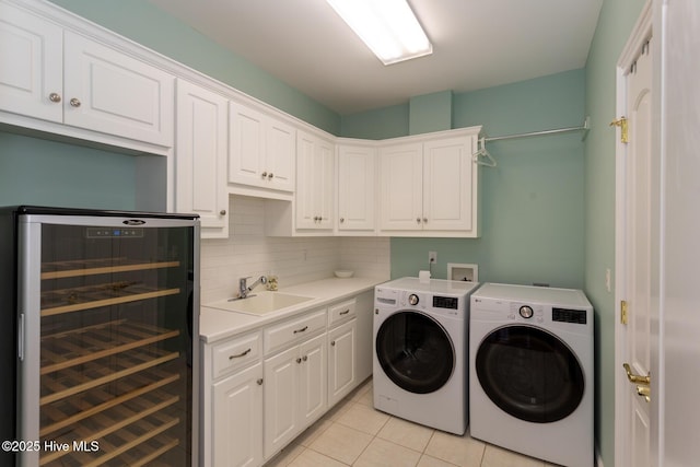 clothes washing area featuring washing machine and dryer, cabinet space, light tile patterned floors, a sink, and wine cooler