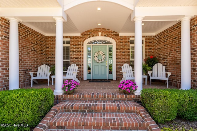 doorway to property featuring a porch and brick siding