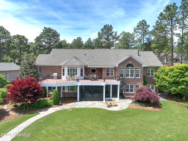 rear view of house featuring a lawn, brick siding, a sunroom, and a patio area
