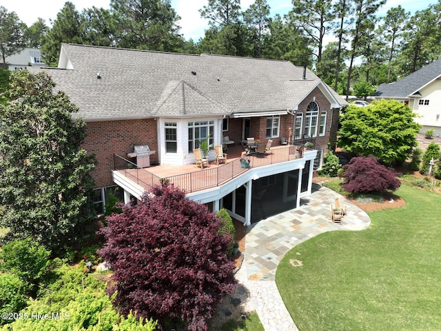 rear view of property featuring a wooden deck, brick siding, a yard, a patio, and a shingled roof