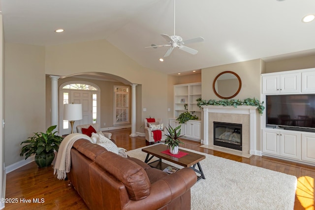 living room featuring a ceiling fan, arched walkways, a fireplace, wood finished floors, and ornate columns