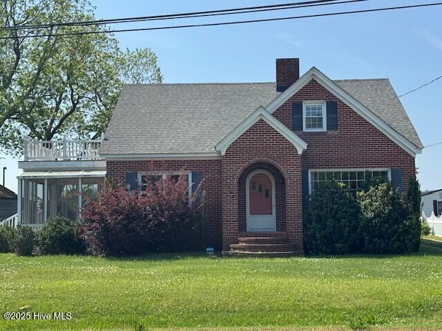 tudor house with brick siding, a front yard, a chimney, and entry steps