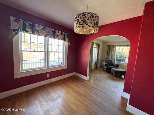 unfurnished dining area with arched walkways, baseboards, visible vents, and wood finished floors