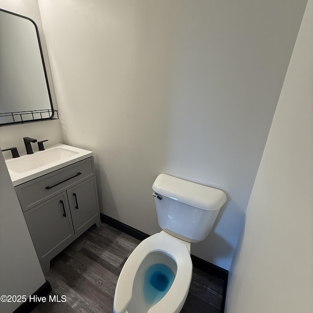 half bathroom with baseboards, wood finished floors, toilet, and vanity