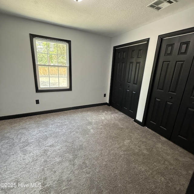 unfurnished bedroom featuring a textured ceiling, multiple closets, carpet, baseboards, and visible vents