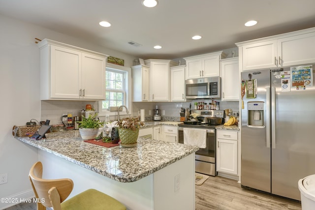 230 Lookout Ln, Sneads Ferry, NC 28460 - kitchen with light stone countertops, a peninsula, a kitchen breakfast bar, stainless steel appliances, and white cabinets