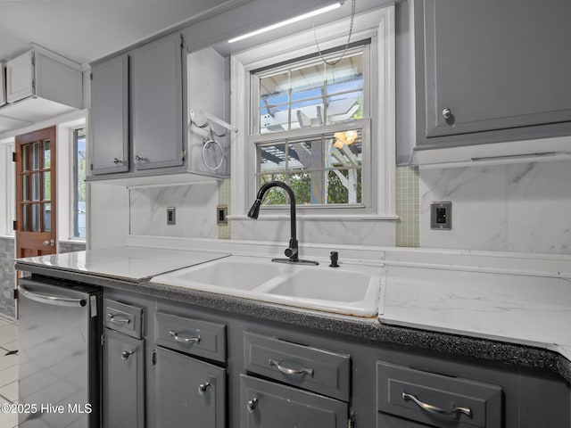 kitchen with gray cabinetry, decorative backsplash, stainless steel dishwasher, and a sink