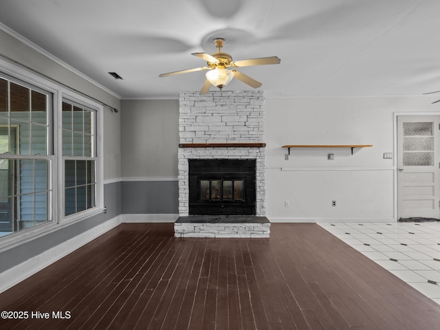 unfurnished living room featuring wood-type flooring, crown molding, ceiling fan, and a stone fireplace