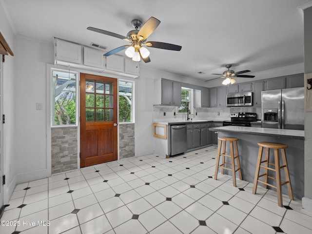 kitchen with visible vents, a kitchen bar, gray cabinets, a ceiling fan, and stainless steel appliances