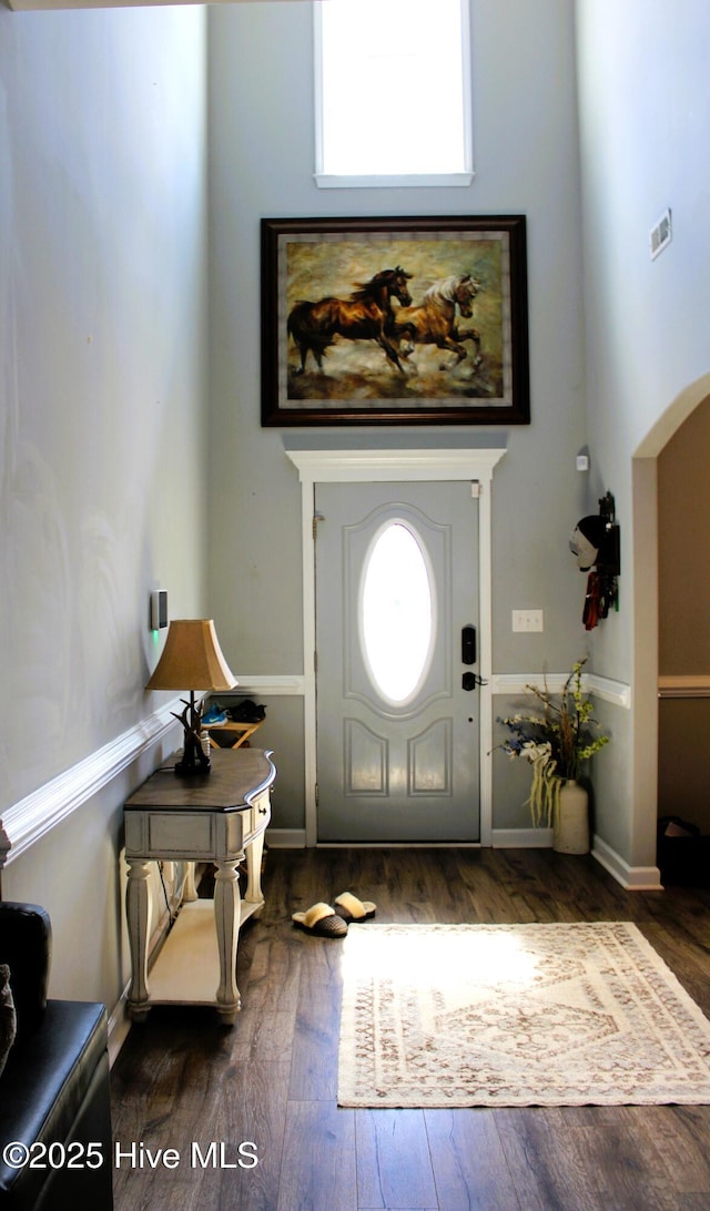 entrance foyer featuring visible vents, arched walkways, and dark wood-style flooring