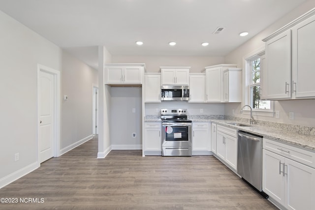kitchen with appliances with stainless steel finishes, a sink, white cabinetry, recessed lighting, and baseboards