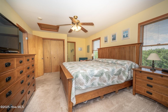 bedroom with ceiling fan, light carpet, a closet, and attic access