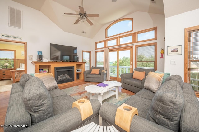 living area with ceiling fan, a fireplace, high vaulted ceiling, light wood-type flooring, and visible vents