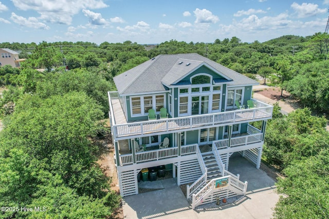 view of front of home featuring a porch, a shingled roof, a view of trees, and stairs