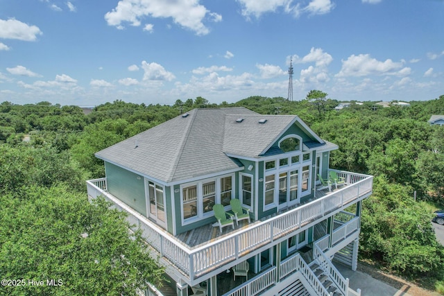 rear view of house featuring a forest view, a shingled roof, and a balcony