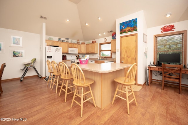 kitchen with visible vents, a kitchen breakfast bar, light brown cabinetry, and white appliances