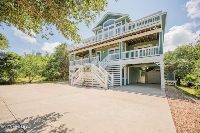 coastal inspired home with stairs, central AC unit, a porch, driveway, and a carport