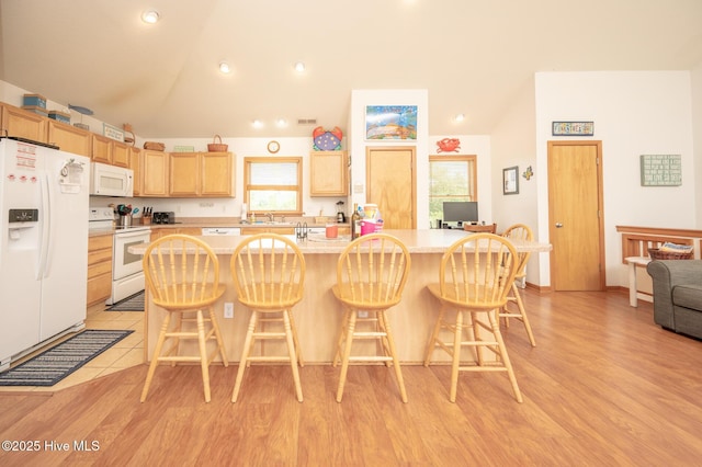 kitchen with a sink, light brown cabinets, vaulted ceiling, and white appliances