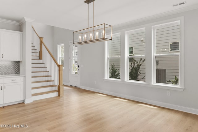 foyer entrance featuring crown molding, an inviting chandelier, light wood-style floors, visible vents, and stairway