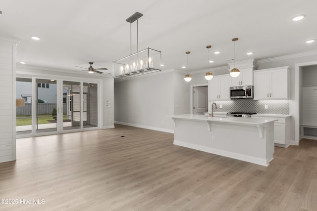kitchen with ceiling fan, crown molding, light countertops, stainless steel microwave, and a breakfast bar
