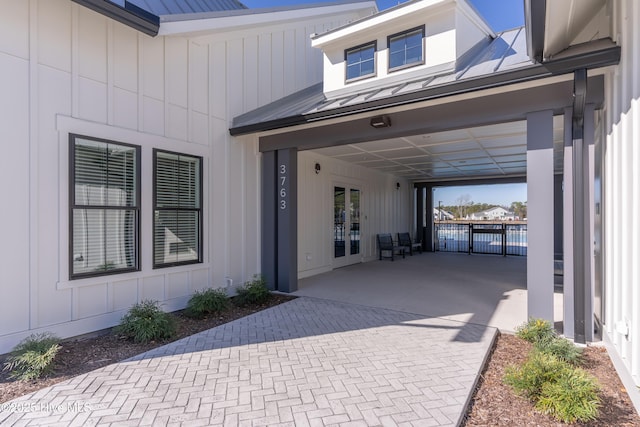 entrance to property with a standing seam roof, french doors, metal roof, fence, and an attached carport