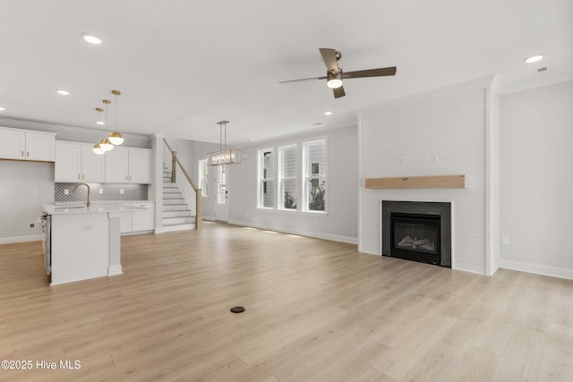 unfurnished living room with ornamental molding, baseboards, recessed lighting, a large fireplace, and ceiling fan with notable chandelier