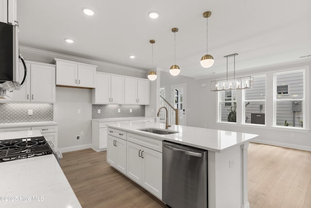 kitchen with white cabinets, appliances with stainless steel finishes, a sink, light wood-style flooring, and backsplash