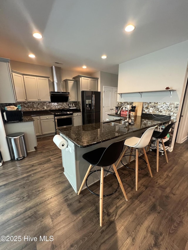 kitchen featuring a sink, a breakfast bar area, black refrigerator with ice dispenser, wall chimney exhaust hood, and gas range