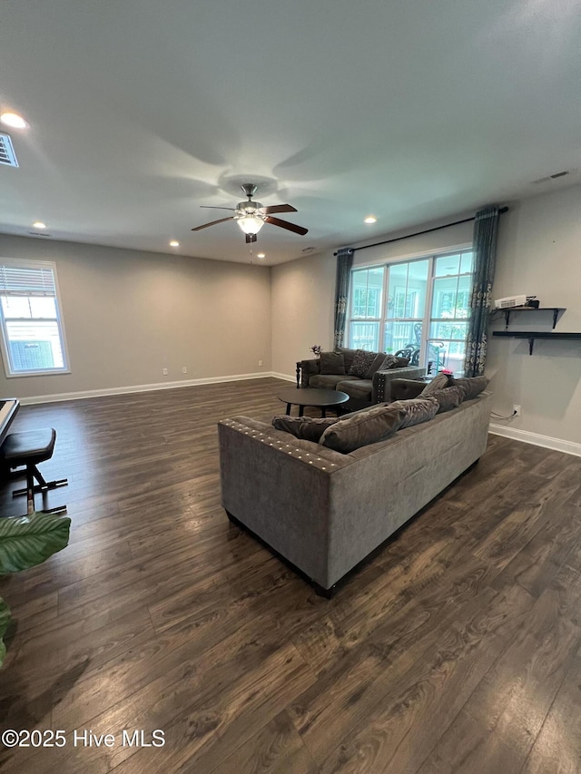 living room featuring dark wood-style flooring, ceiling fan, visible vents, and baseboards