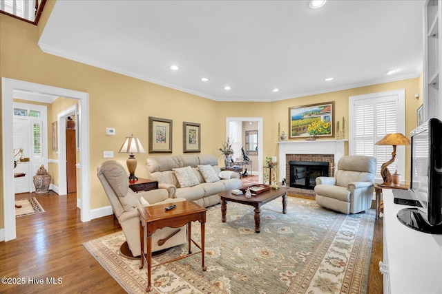 living room featuring recessed lighting, baseboards, wood finished floors, crown molding, and a brick fireplace