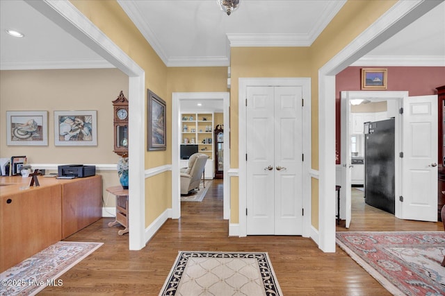 entryway with wood finished floors, ornamental molding, and baseboards