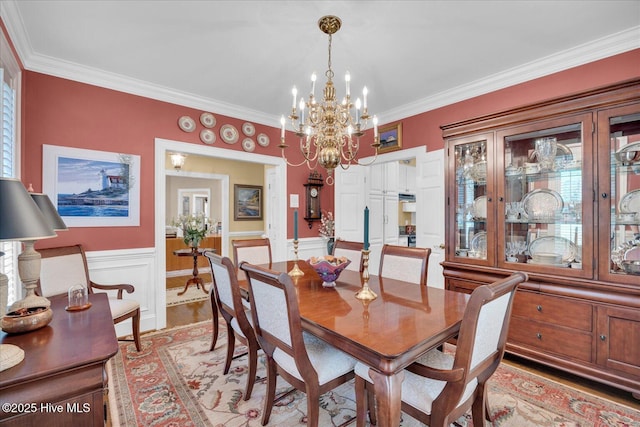 dining room with a chandelier, crown molding, and a wainscoted wall