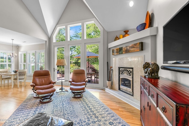 living area with a premium fireplace, high vaulted ceiling, a notable chandelier, and light wood-type flooring