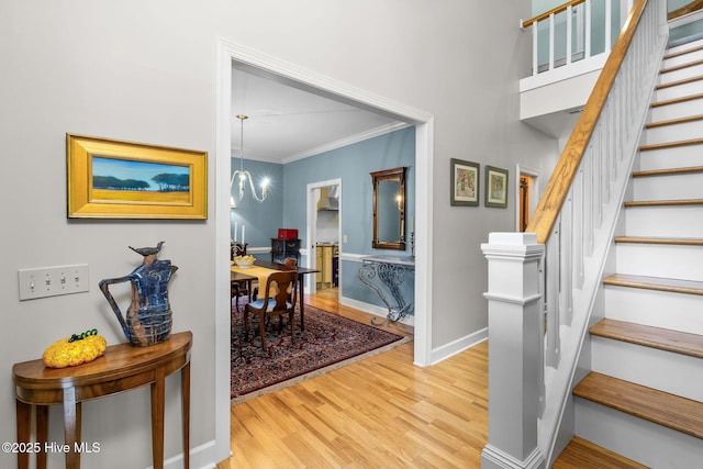 stairs featuring crown molding, baseboards, wood finished floors, and a notable chandelier