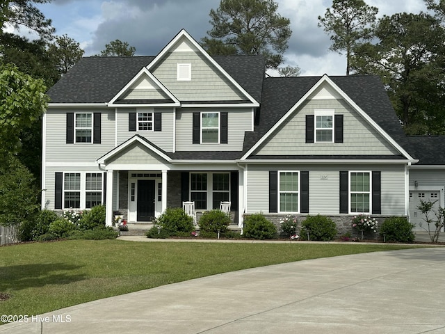 craftsman inspired home with a shingled roof, a porch, stone siding, and a front yard