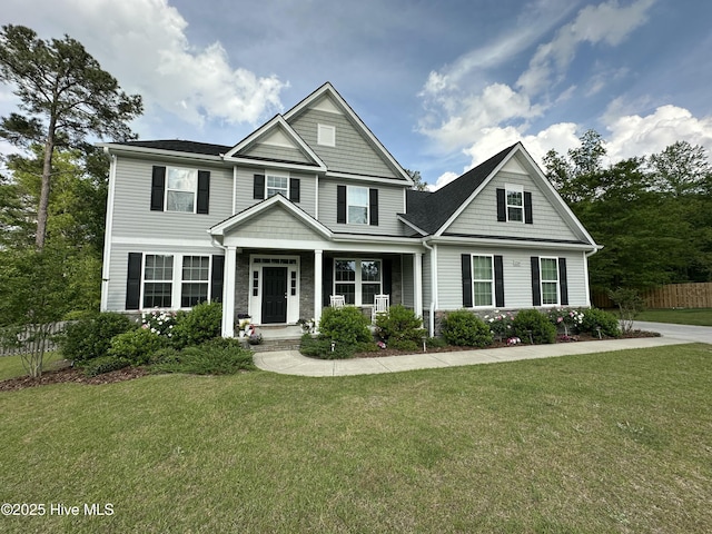craftsman-style house with covered porch, fence, stone siding, and a front lawn