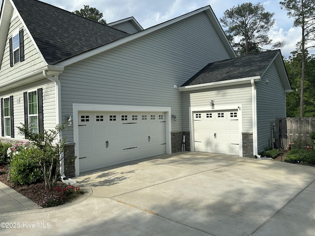 view of property exterior featuring fence, stone siding, roof with shingles, concrete driveway, and an attached garage