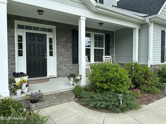 entrance to property with covered porch, roof with shingles, and stone siding