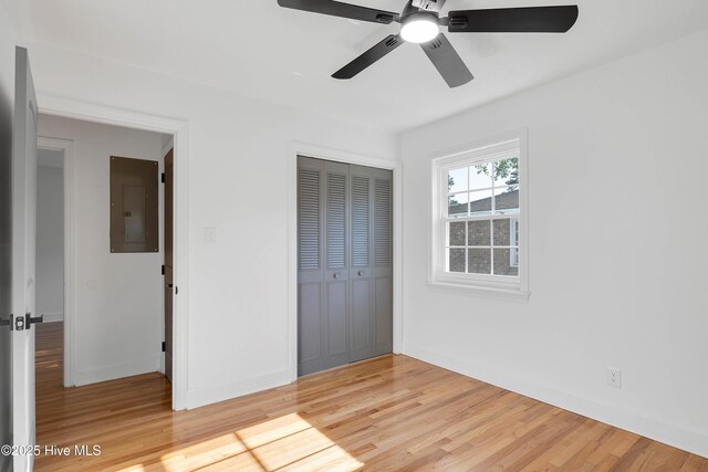 unfurnished bedroom featuring ceiling fan, electric panel, light wood-style floors, baseboards, and a closet