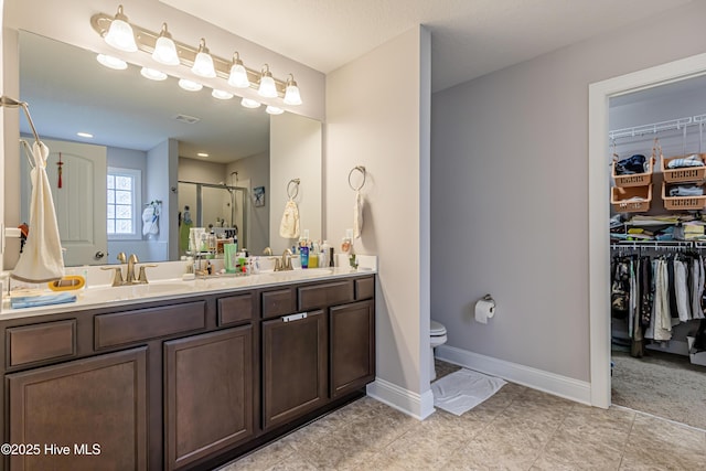 full bath with double vanity, toilet, a walk in closet, a sink, and a stall shower