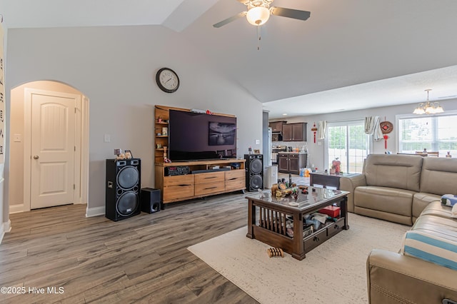 living room featuring arched walkways, ceiling fan with notable chandelier, baseboards, wood finished floors, and vaulted ceiling