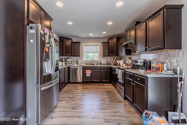kitchen featuring dark brown cabinetry, a sink, stainless steel appliances, recessed lighting, and light wood-style flooring