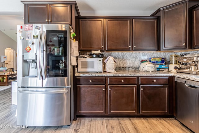 kitchen with stainless steel appliances, light stone counters, tasteful backsplash, and dark brown cabinets