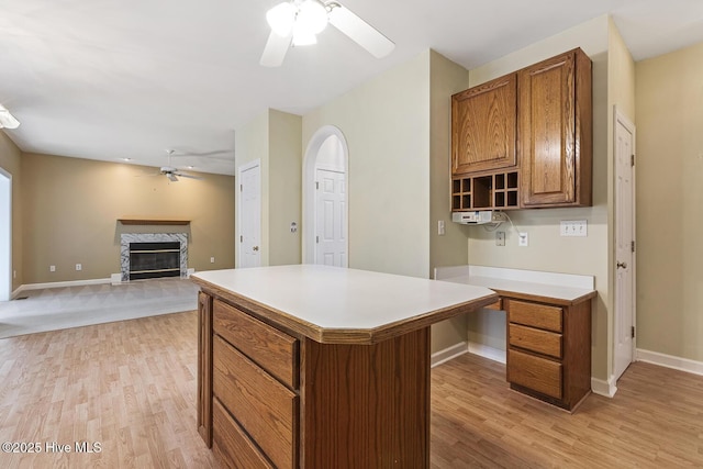 1601 Castalia Dr, Cary, NC 27513 - kitchen with ceiling fan, light wood-type flooring, brown cabinets, a glass covered fireplace, and light countertops